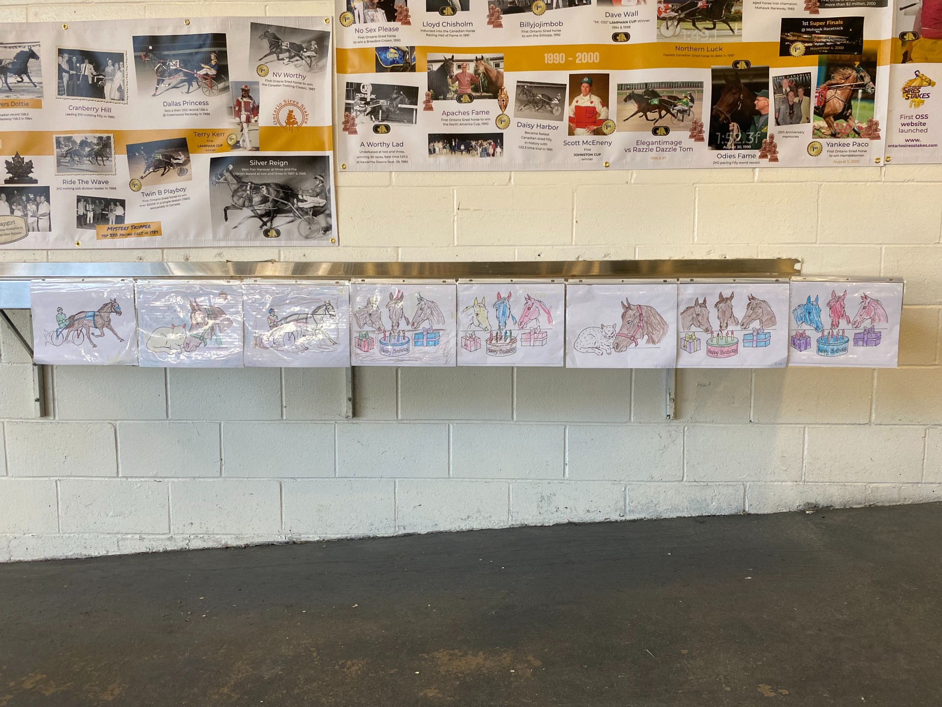 Kids’ colouring pages are displayed underneath the OSS 50th Anniversary timeline at Dresden Raceway on Monday, July 1, 2024 (Ontario Sires Stakes)